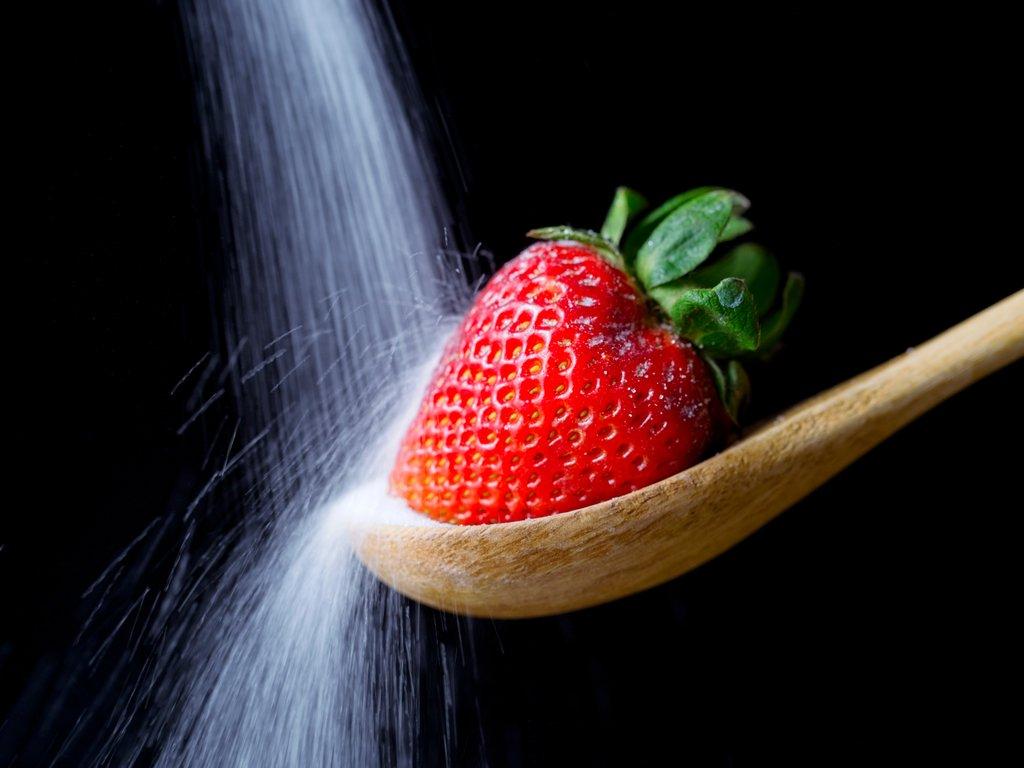 Sugar pouring on a strawberry on wooden spoon